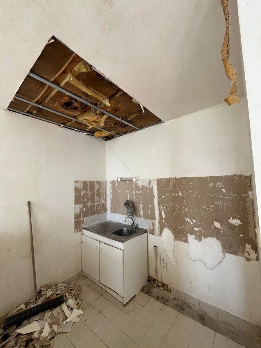 Kitchen tile removal and strip-out in progress at a Brighton property — wall tiles removed, ceiling opened for leak investigation