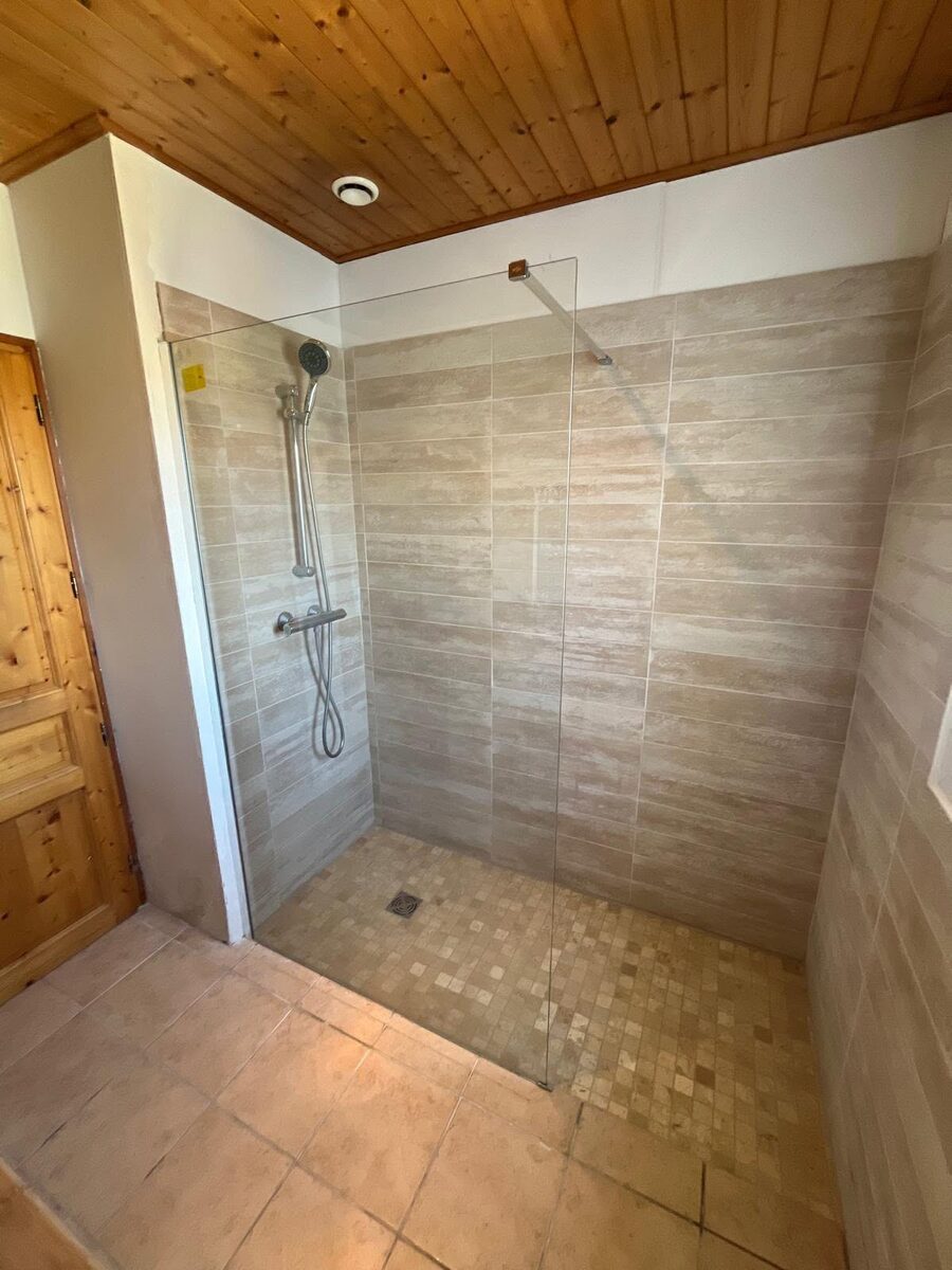 Completed walk-in shower with stone-effect tiles, frameless glass panel and rainfall shower in a Brighton property